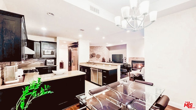 kitchen featuring a multi sided fireplace, appliances with stainless steel finishes, pendant lighting, sink, and kitchen peninsula