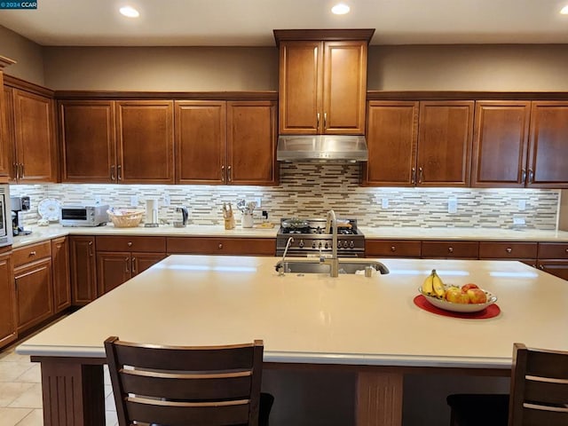 kitchen with stainless steel microwave, an island with sink, a kitchen bar, decorative backsplash, and light tile patterned flooring