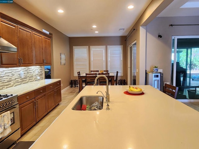 kitchen featuring ventilation hood, sink, stainless steel gas range, decorative backsplash, and light tile patterned floors