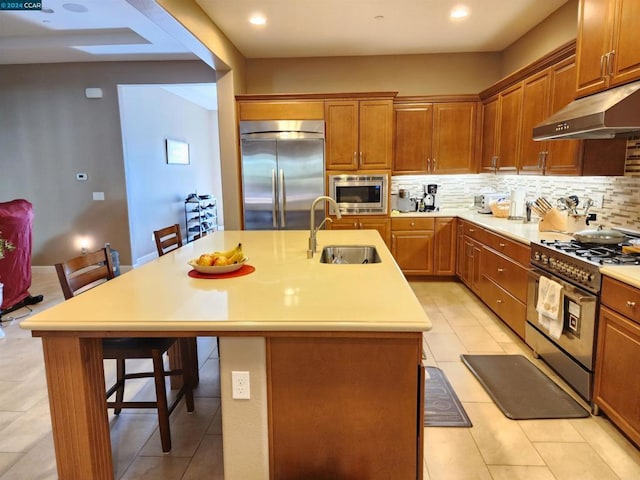 kitchen with a kitchen breakfast bar, built in appliances, a kitchen island with sink, and sink