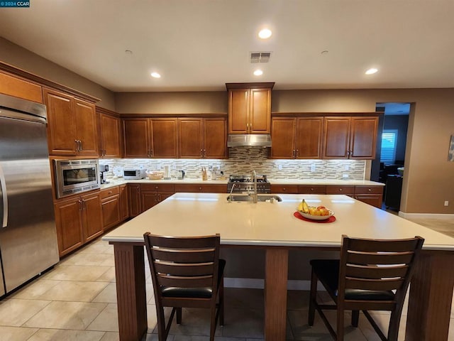 kitchen with built in appliances, a breakfast bar, sink, and an island with sink