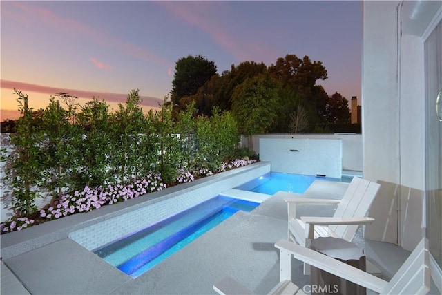 pool at dusk featuring an in ground hot tub