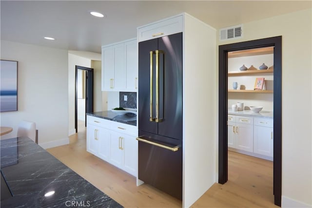 kitchen with white cabinets, light hardwood / wood-style floors, high end fridge, and dark stone countertops