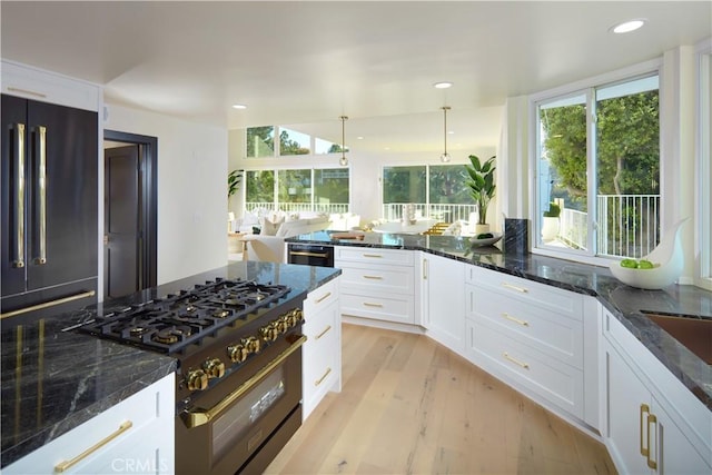 kitchen with dark stone counters, black stovetop, light hardwood / wood-style flooring, decorative light fixtures, and white cabinetry