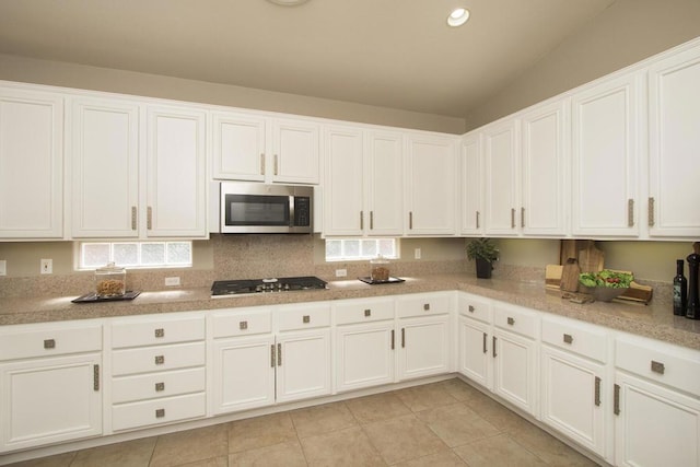 kitchen featuring white cabinetry, stainless steel appliances, backsplash, light tile patterned flooring, and vaulted ceiling