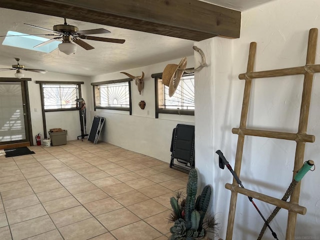 interior space featuring light tile patterned floors, ceiling fan, plenty of natural light, and vaulted ceiling with skylight