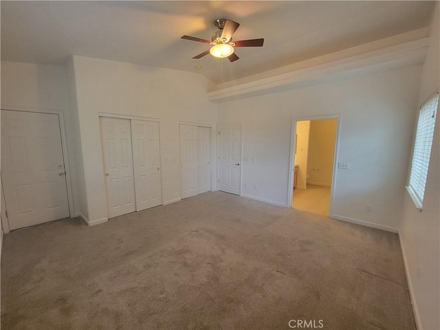 unfurnished bedroom with ceiling fan, two closets, light colored carpet, and ensuite bath