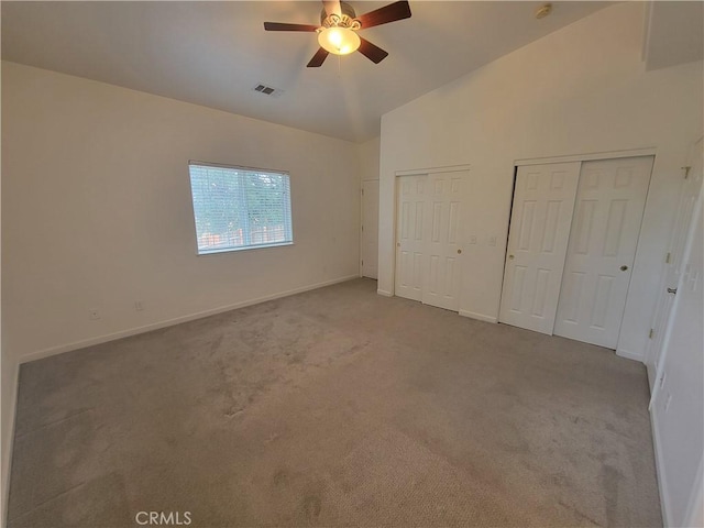 unfurnished bedroom featuring two closets, light colored carpet, vaulted ceiling, and ceiling fan