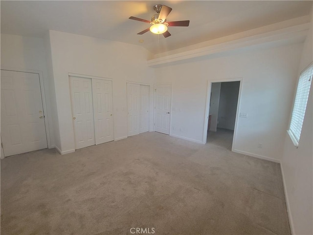 unfurnished bedroom with multiple closets, ceiling fan, and light carpet