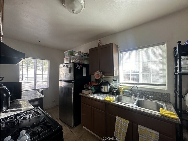 kitchen with exhaust hood, stainless steel fridge, light tile patterned flooring, black gas range, and sink