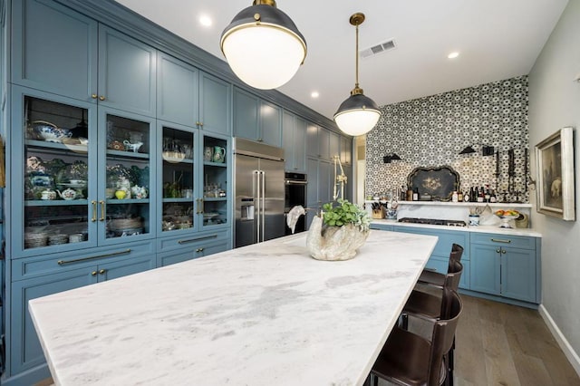 kitchen featuring blue cabinetry, hanging light fixtures, stainless steel appliances, dark wood-type flooring, and backsplash