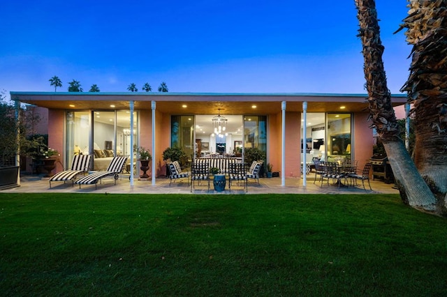 back house at dusk featuring a lawn and a patio area