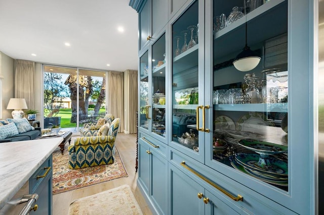 bar featuring light wood-type flooring, light stone countertops, and blue cabinets