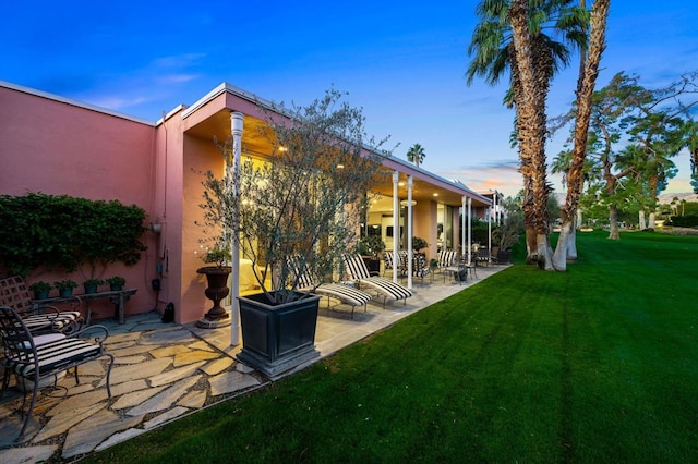 back house at dusk featuring a patio area and a lawn