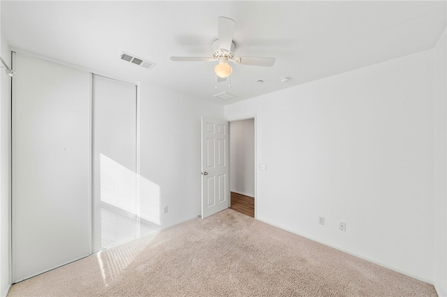 unfurnished bedroom with a closet, light colored carpet, and ceiling fan