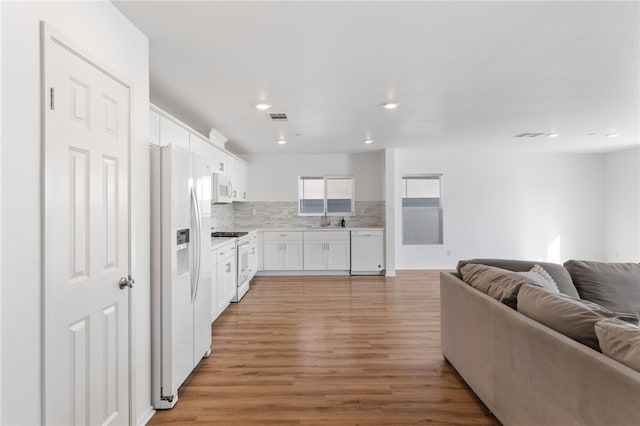 kitchen with tasteful backsplash, white appliances, sink, white cabinets, and light hardwood / wood-style floors