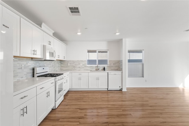 kitchen featuring light wood-type flooring, backsplash, white appliances, sink, and white cabinetry