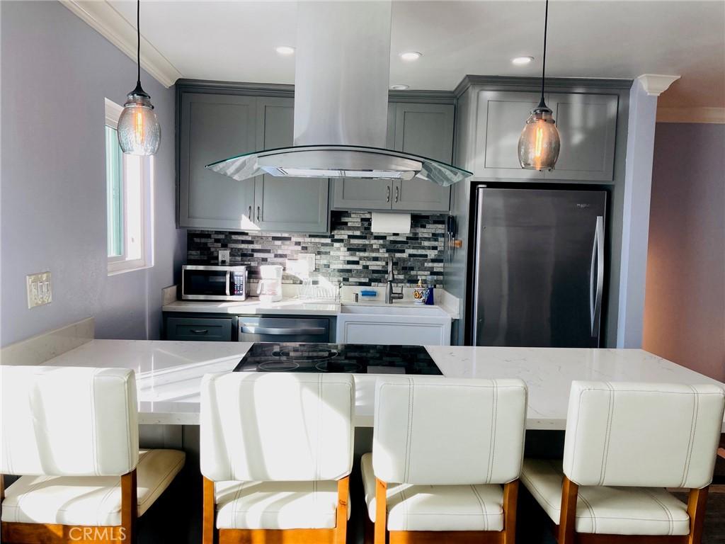 kitchen featuring stainless steel appliances, island exhaust hood, pendant lighting, gray cabinets, and ornamental molding