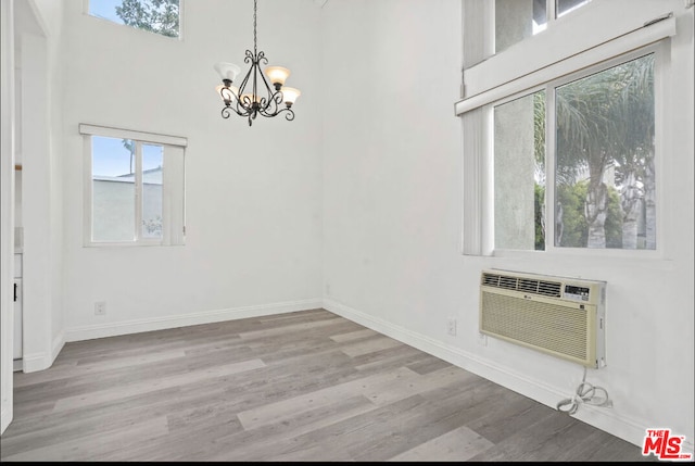 unfurnished dining area with a wall mounted air conditioner, a notable chandelier, light wood-type flooring, and a towering ceiling