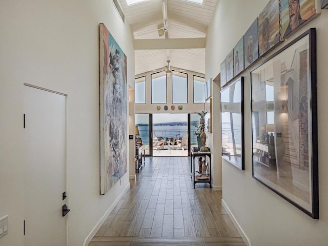 hall with a water view, a skylight, high vaulted ceiling, dark hardwood / wood-style flooring, and beam ceiling