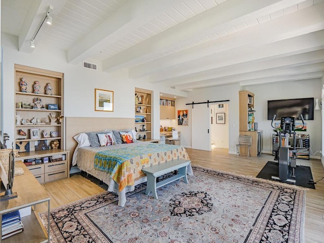 bedroom with rail lighting, light hardwood / wood-style flooring, a barn door, and beamed ceiling