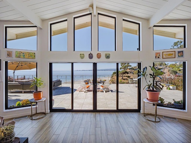 entryway with a water view, wood-type flooring, and vaulted ceiling with beams