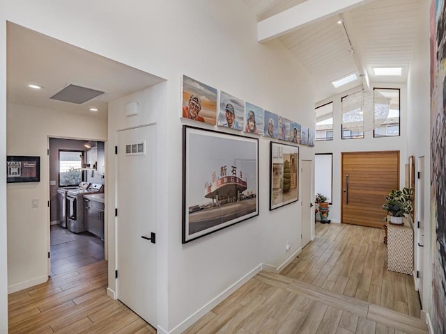 hallway featuring washer / dryer, light hardwood / wood-style flooring, high vaulted ceiling, and beamed ceiling