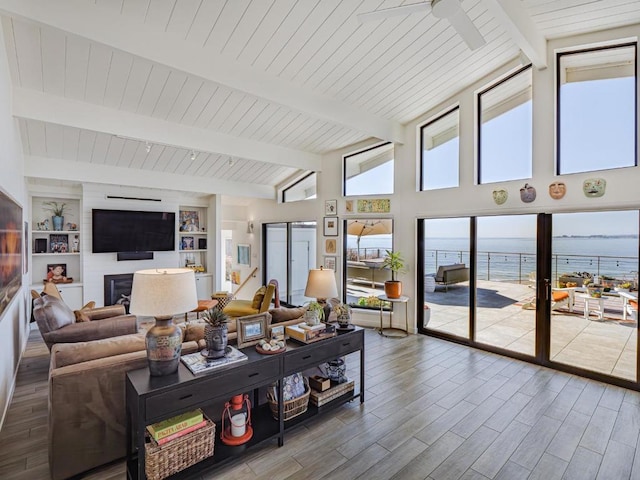 living room featuring vaulted ceiling with beams, a water view, a large fireplace, built in features, and hardwood / wood-style floors