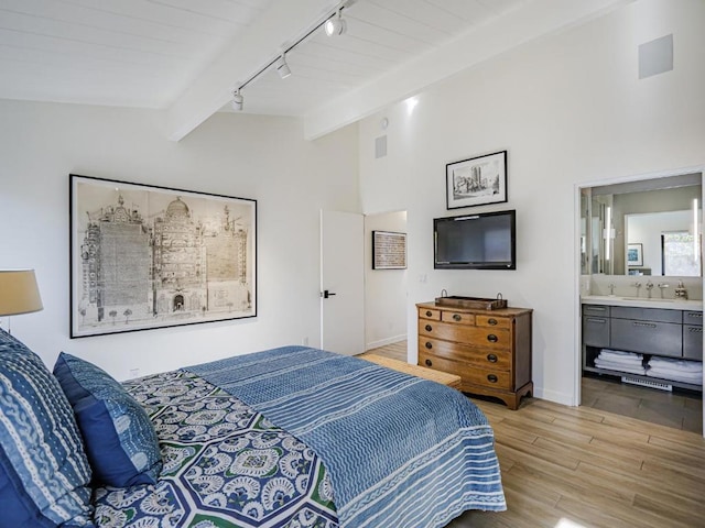 bedroom featuring ensuite bathroom, rail lighting, sink, lofted ceiling with beams, and light wood-type flooring