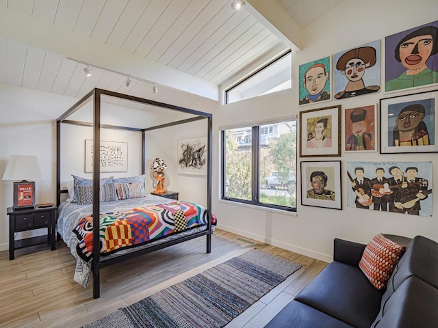 bedroom featuring wood ceiling, rail lighting, lofted ceiling with beams, and light hardwood / wood-style floors