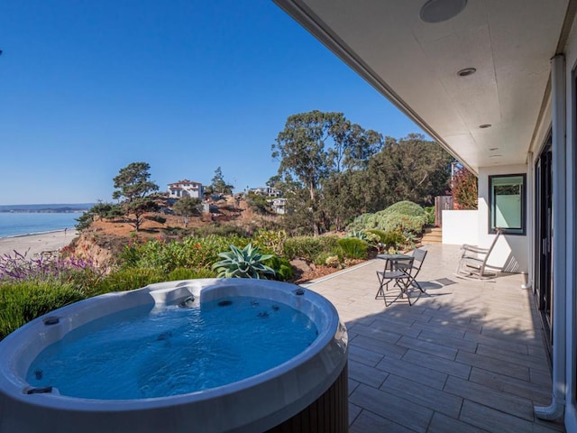 view of patio featuring an outdoor hot tub and a water view