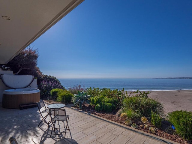 view of patio / terrace featuring a hot tub, a water view, and a view of the beach