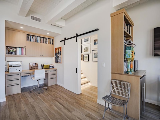 office featuring beamed ceiling, a barn door, built in desk, and light wood-type flooring