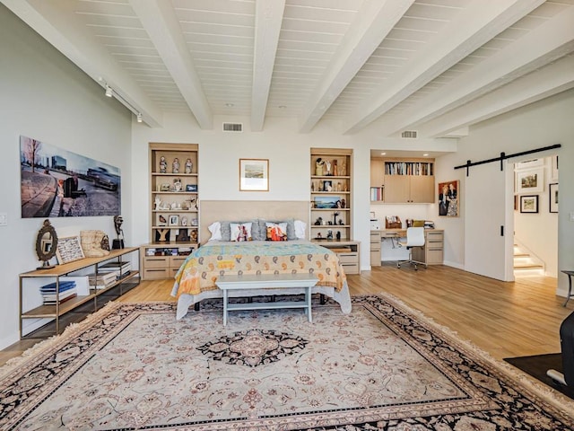 bedroom featuring a barn door, beam ceiling, and light wood-type flooring