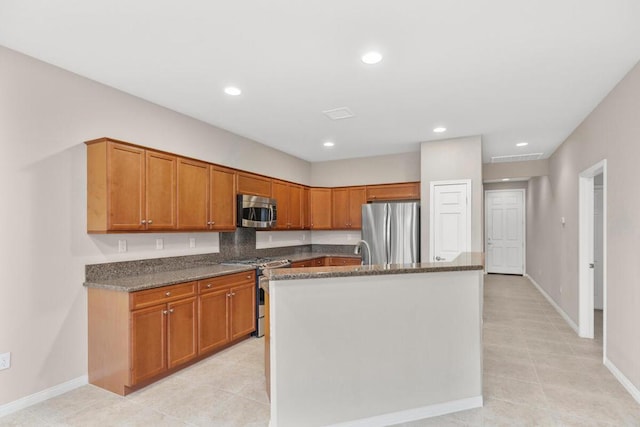 kitchen featuring appliances with stainless steel finishes, dark stone countertops, sink, light tile patterned floors, and a center island with sink