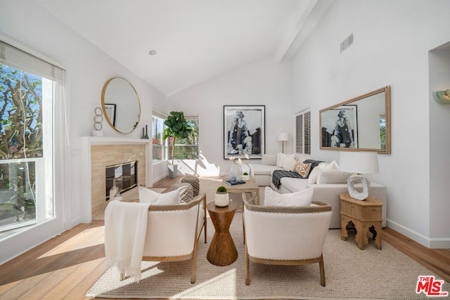 living room featuring beamed ceiling, high vaulted ceiling, light wood-type flooring, and a tile fireplace