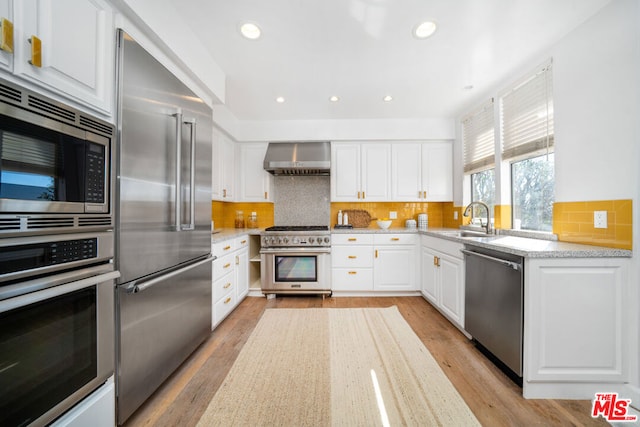 kitchen featuring built in appliances, wall chimney exhaust hood, decorative backsplash, light wood-type flooring, and white cabinetry