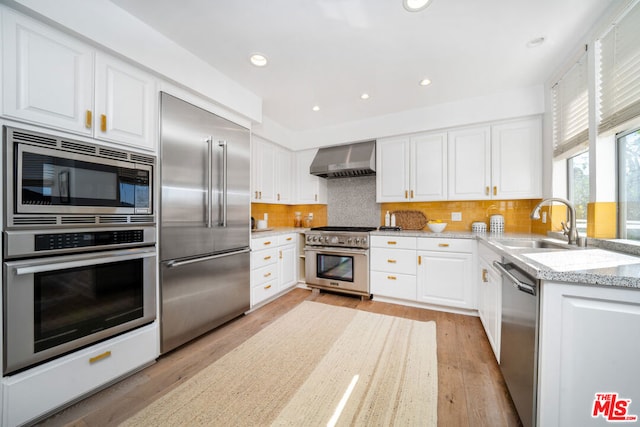 kitchen with built in appliances, light hardwood / wood-style floors, white cabinetry, and wall chimney exhaust hood