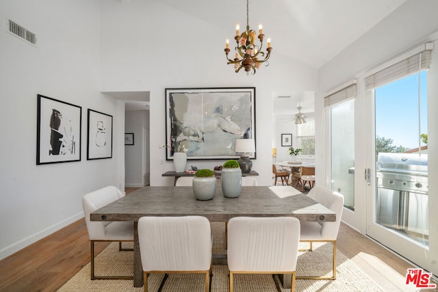 dining space with ceiling fan with notable chandelier, lofted ceiling, and light hardwood / wood-style flooring