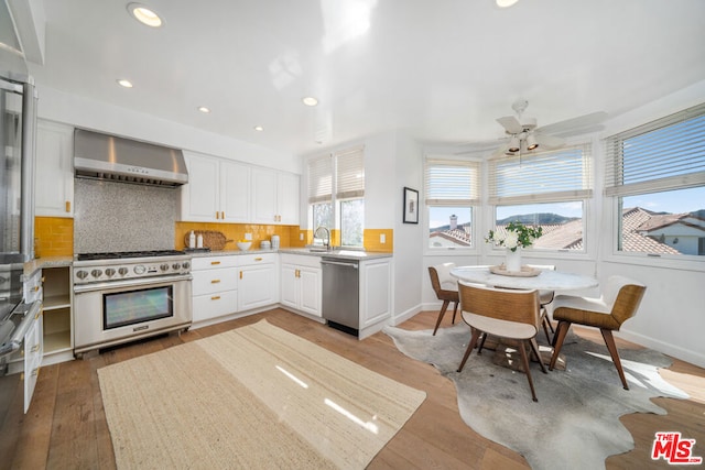 kitchen with backsplash, hardwood / wood-style flooring, wall chimney exhaust hood, appliances with stainless steel finishes, and white cabinetry