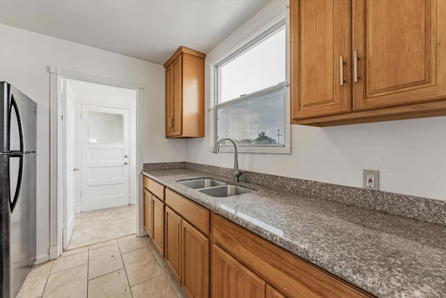 kitchen with light tile patterned floors, sink, stainless steel refrigerator, and dark stone counters