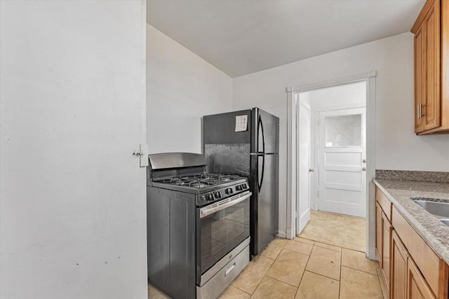 kitchen with stainless steel gas range oven, black fridge, and light tile patterned flooring