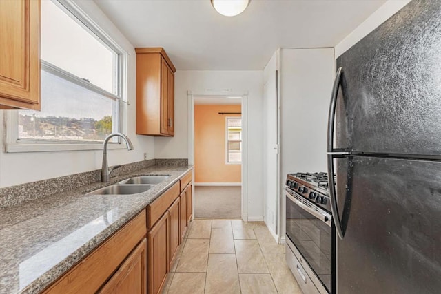 kitchen with light stone countertops, black fridge, sink, light tile patterned floors, and stainless steel range with gas stovetop