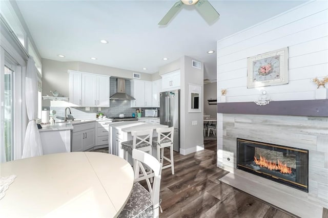 kitchen with white cabinets, wall chimney exhaust hood, dark hardwood / wood-style floors, decorative backsplash, and stainless steel refrigerator