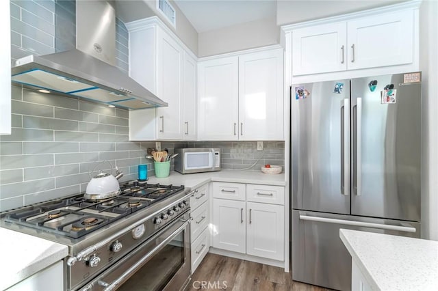 kitchen with wall chimney exhaust hood, white cabinetry, decorative backsplash, and stainless steel appliances