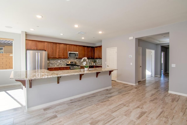 kitchen with a spacious island, a breakfast bar area, light hardwood / wood-style floors, light stone counters, and stainless steel appliances