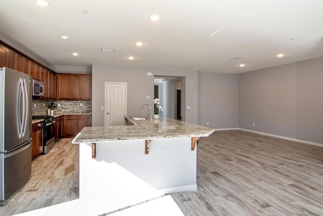 kitchen featuring a kitchen breakfast bar, sink, light wood-type flooring, a large island, and stainless steel appliances