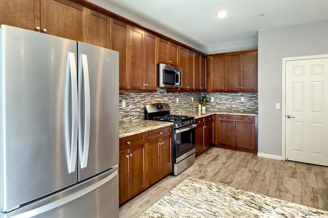 kitchen with backsplash, light stone countertops, stainless steel appliances, and light wood-type flooring