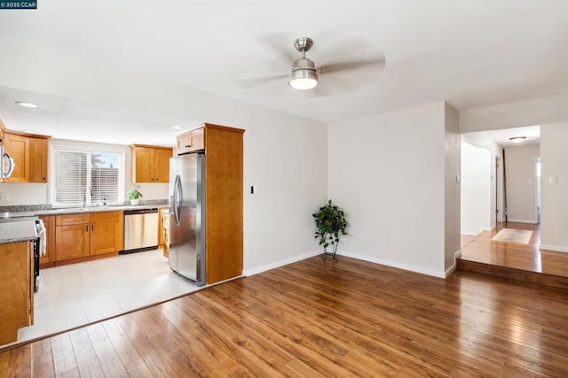 kitchen featuring ceiling fan, appliances with stainless steel finishes, light stone countertops, and light wood-type flooring