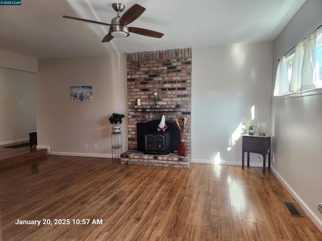 unfurnished living room with hardwood / wood-style flooring, a wood stove, and ceiling fan